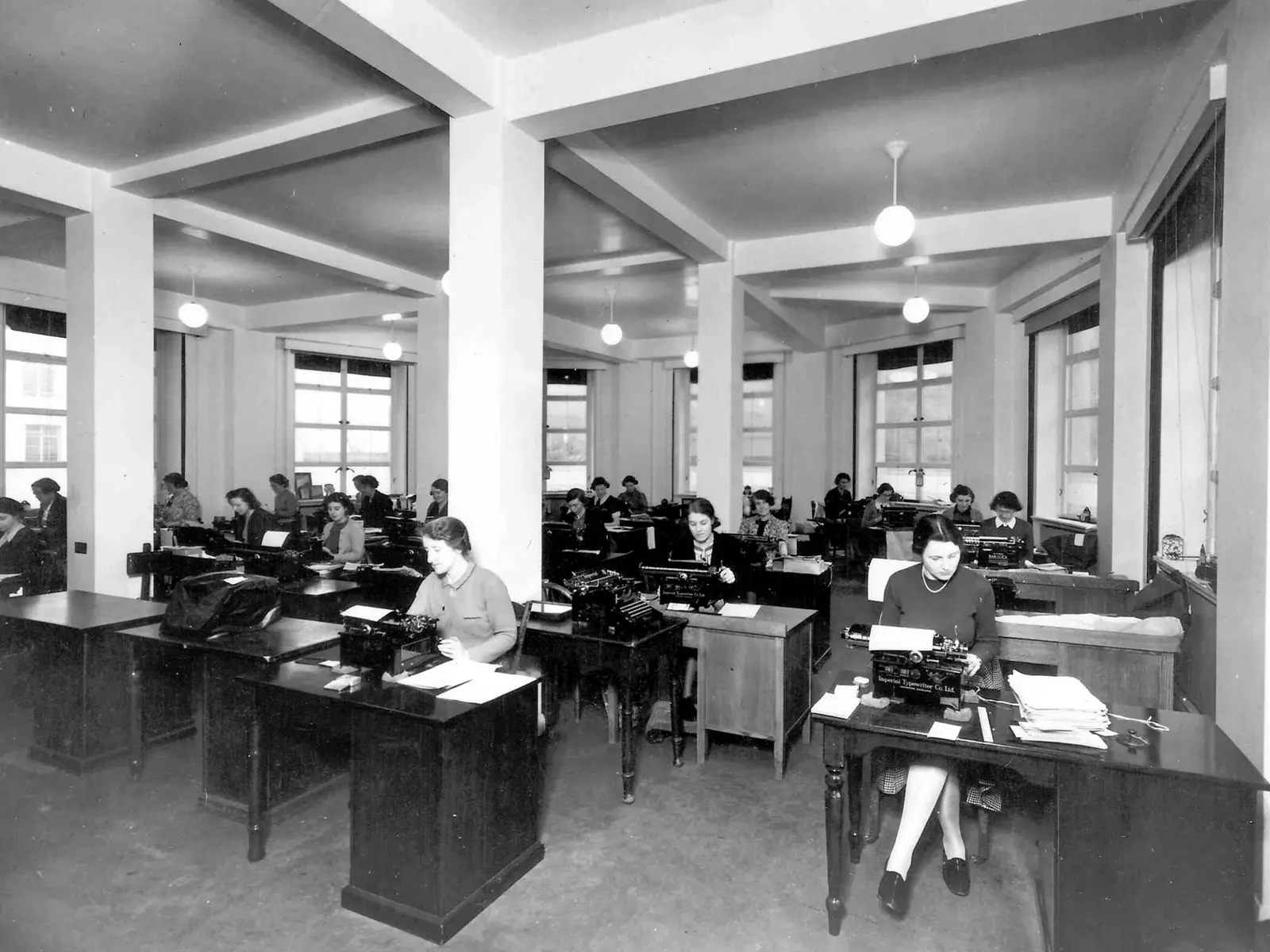 A typing pool: rows of typists at desks in a large office